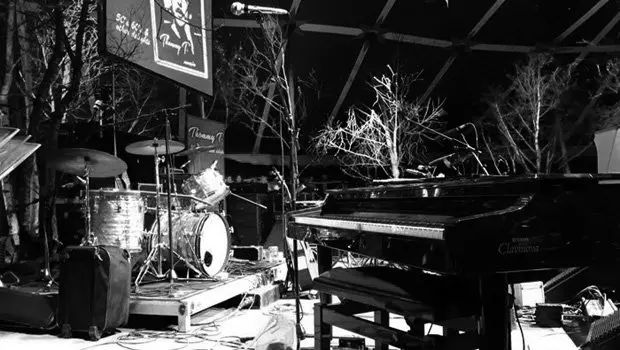 Schwarzweißbild mit Klavier, Schlagzeug, Mikrofonen und Bühnenzubehör auf einer kleinen überdachten Bühne für einen Auftritt der Band Thommy T. (alias Thomas Klemt) and friends.